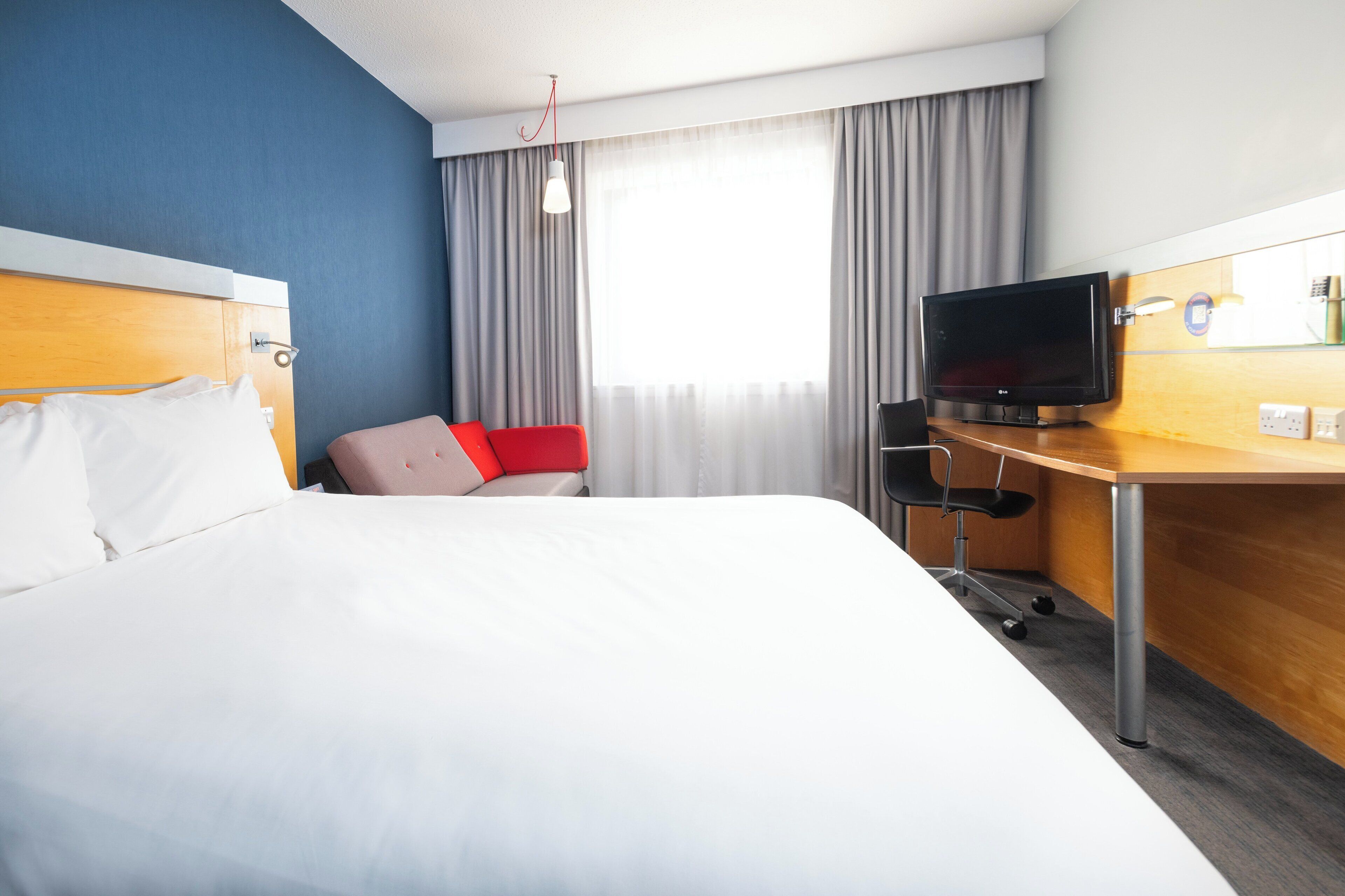 Una camera d'albergo con un letto, una scrivania con televisione e una finestra con tende.
