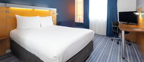 Habitación de hotel con una cama grande, un escritorio con silla, un televisor de pantalla plana y una ventana con cortinas.