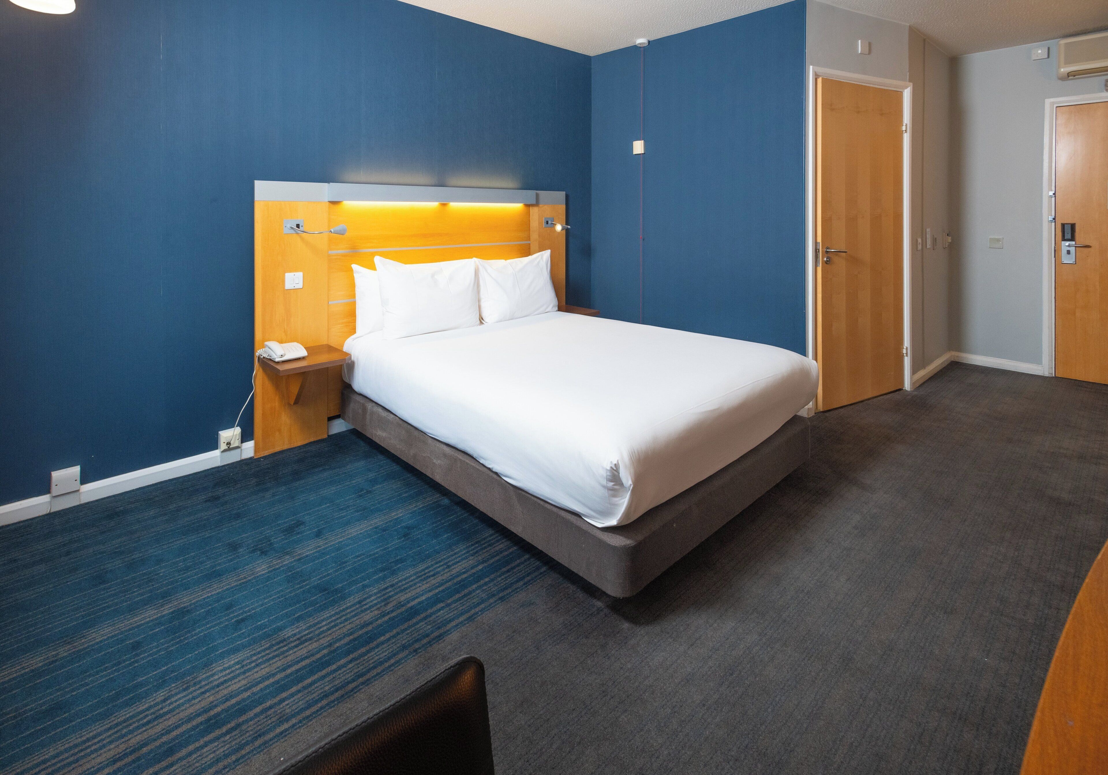 A hotel room with a bed, bedside table, and a desk.