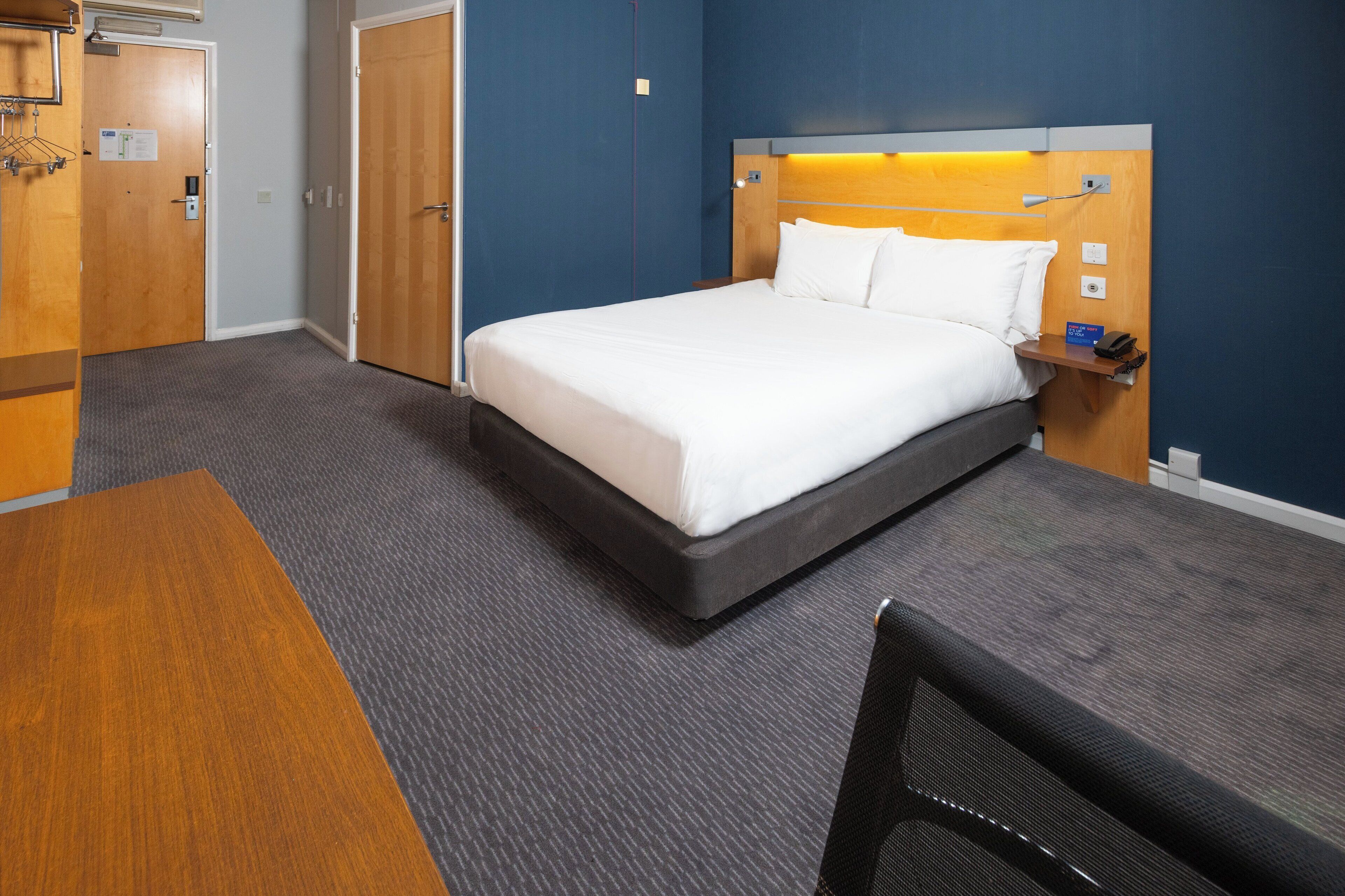 A hotel room with a bed, a desk, a chair, a nightstand, and a wardrobe.