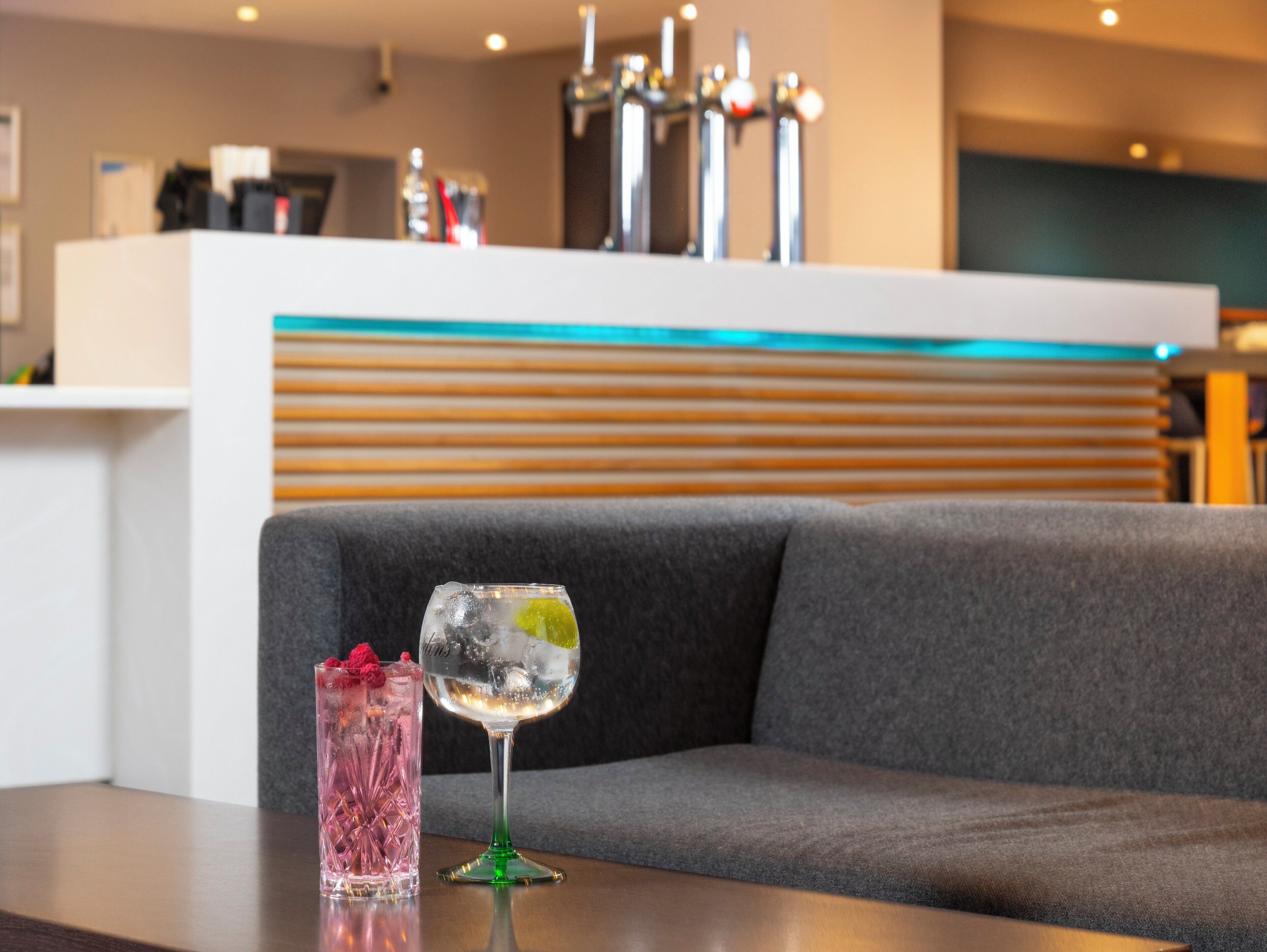 A bar area with two glasses of beverages on a table, a bar counter, and a seating area with a sofa.