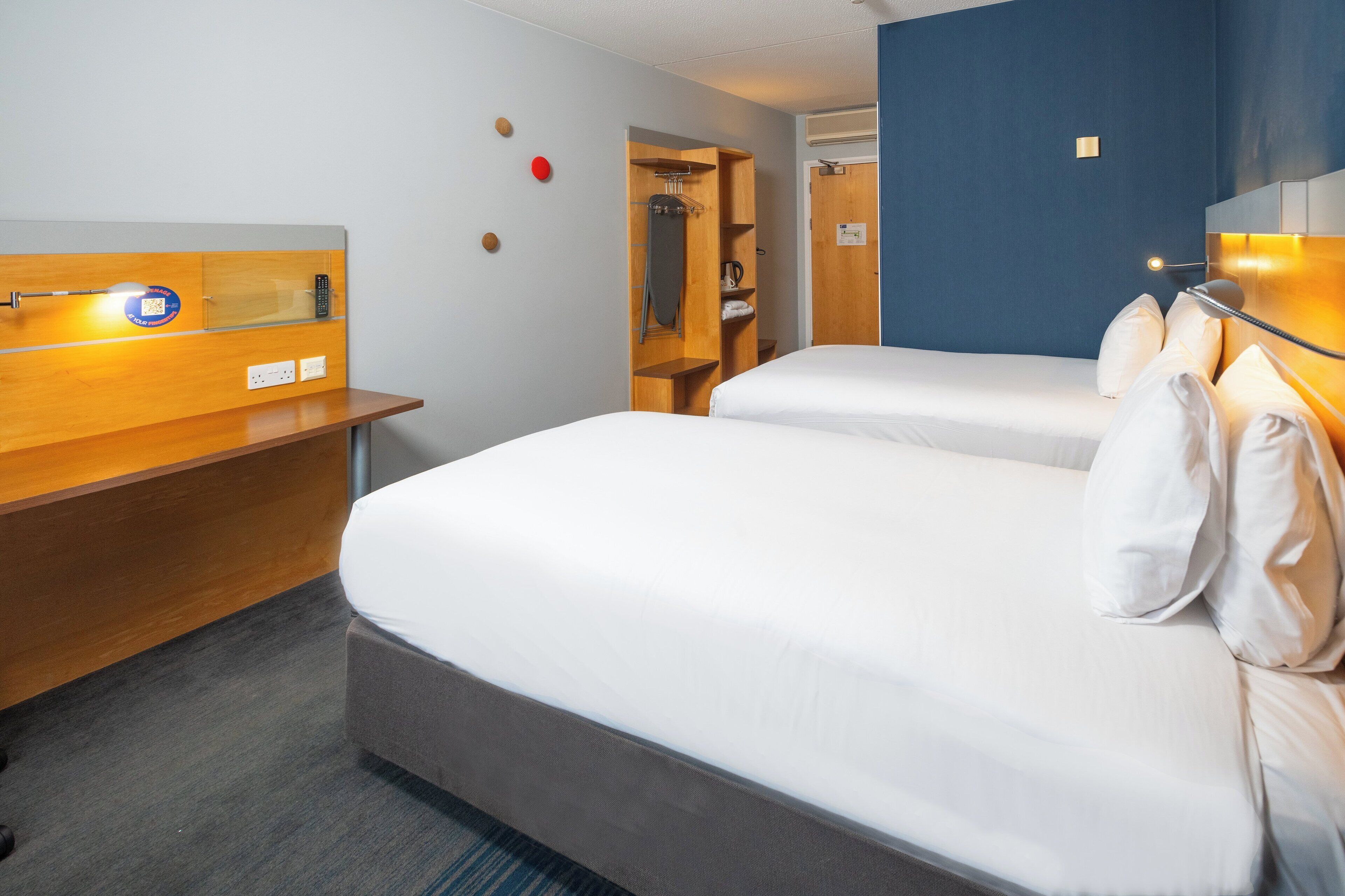 A hotel room with two beds, a wooden desk, a wardrobe, and a mirror.
