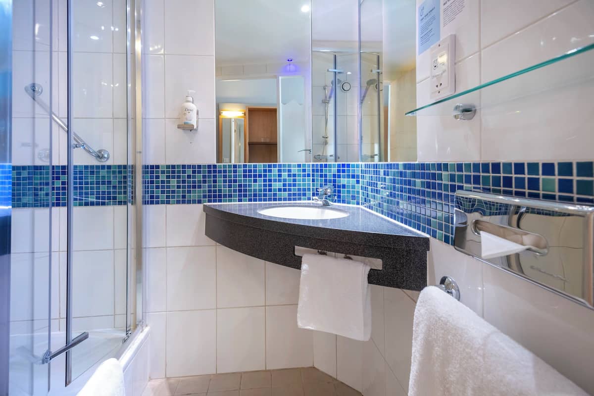 A modern bathroom with a glass shower enclosure, a sink with a black countertop, and a mirror with a glass shelf.
