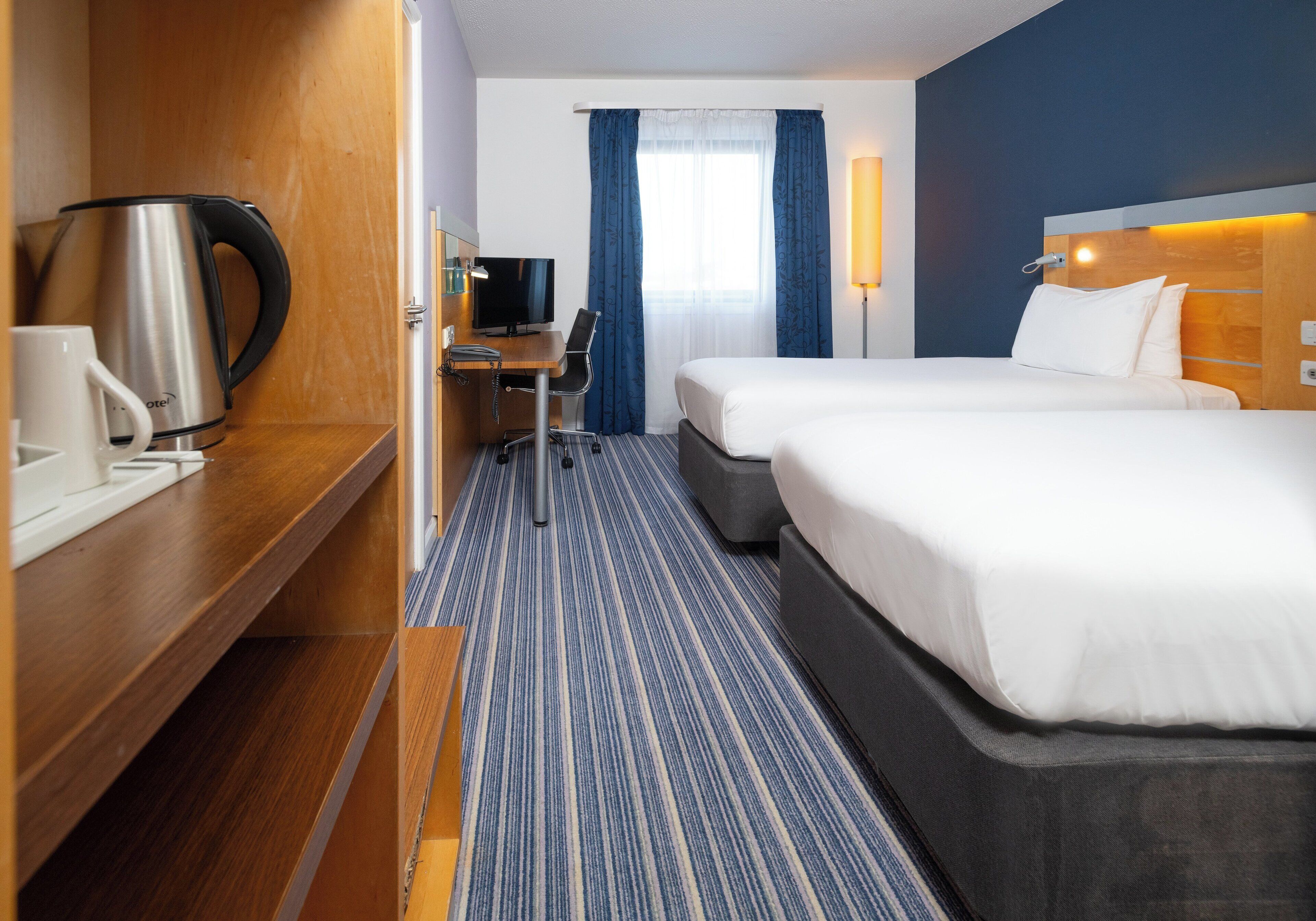 A hotel room with a bed, a desk with a chair, a coffee maker, and a television.