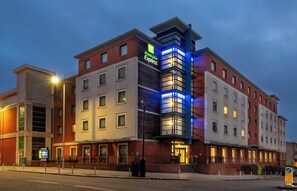 A Holiday Inn Express hotel with a modern design, featuring a prominent corner entrance and a mix of brick and glass facades. - Holiday Inn Express Stevenage by IHG (Stevenage)