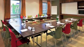 A conference room with a long table, multiple chairs, a projector screen, and a whiteboard.
