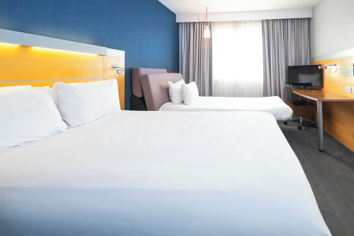 A hotel room with two beds, a desk, a television, and a window with curtains.