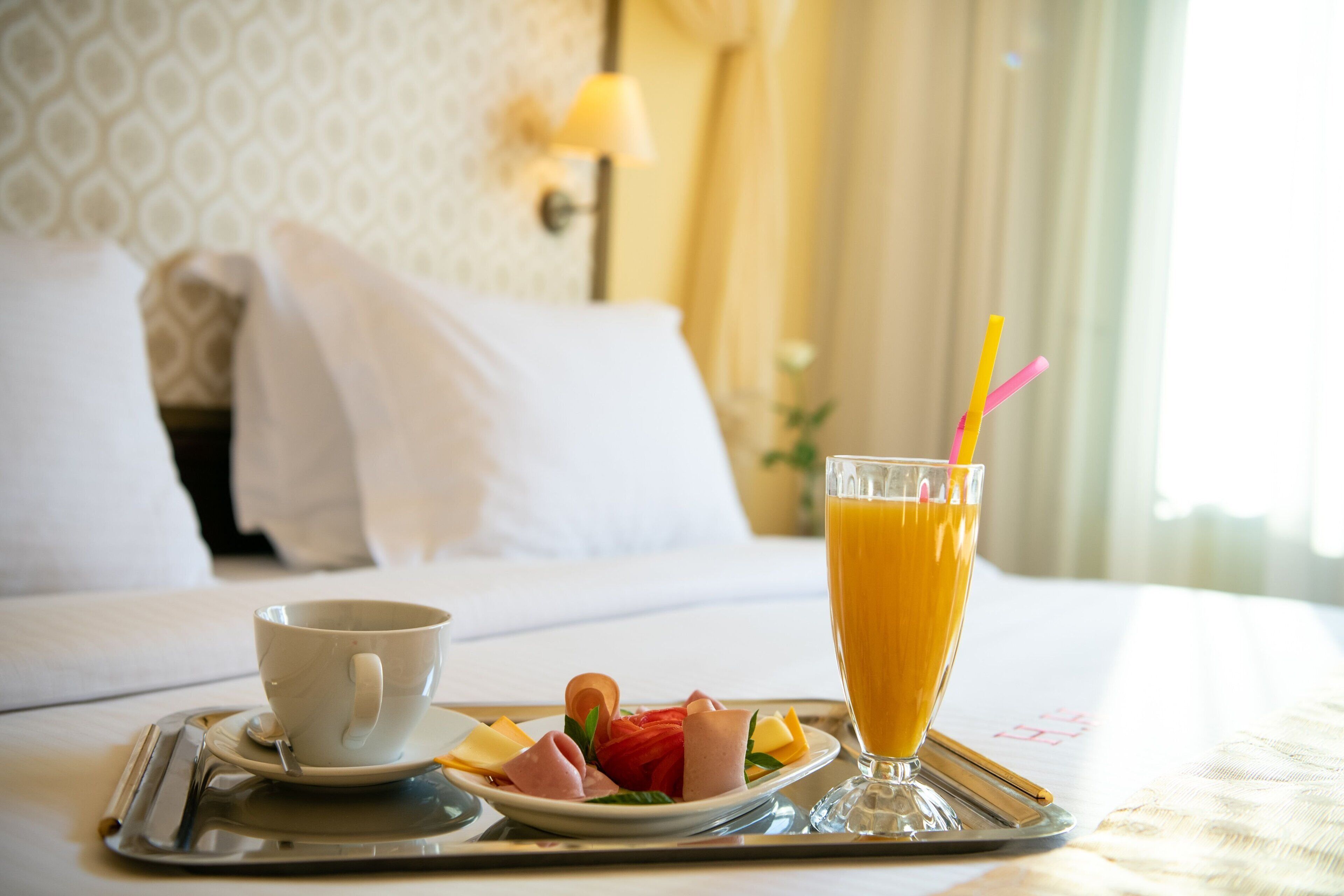 Bandeja de desayuno con una taza de café, un vaso de zumo de naranja y un plato con diversas opciones de comida sobre una cama de hotel.