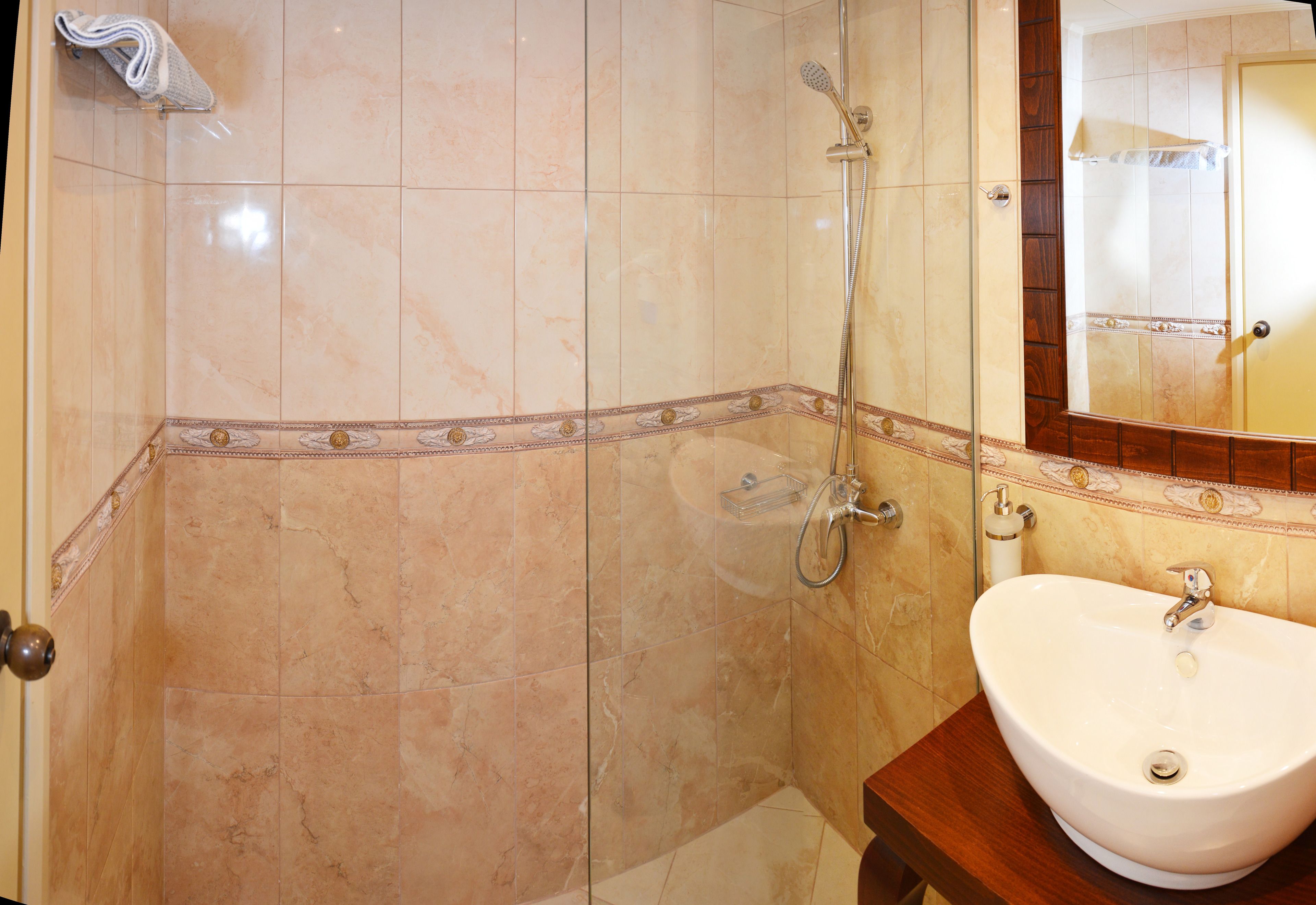 A bathroom with a sink, mirror, shower, and tiled walls.