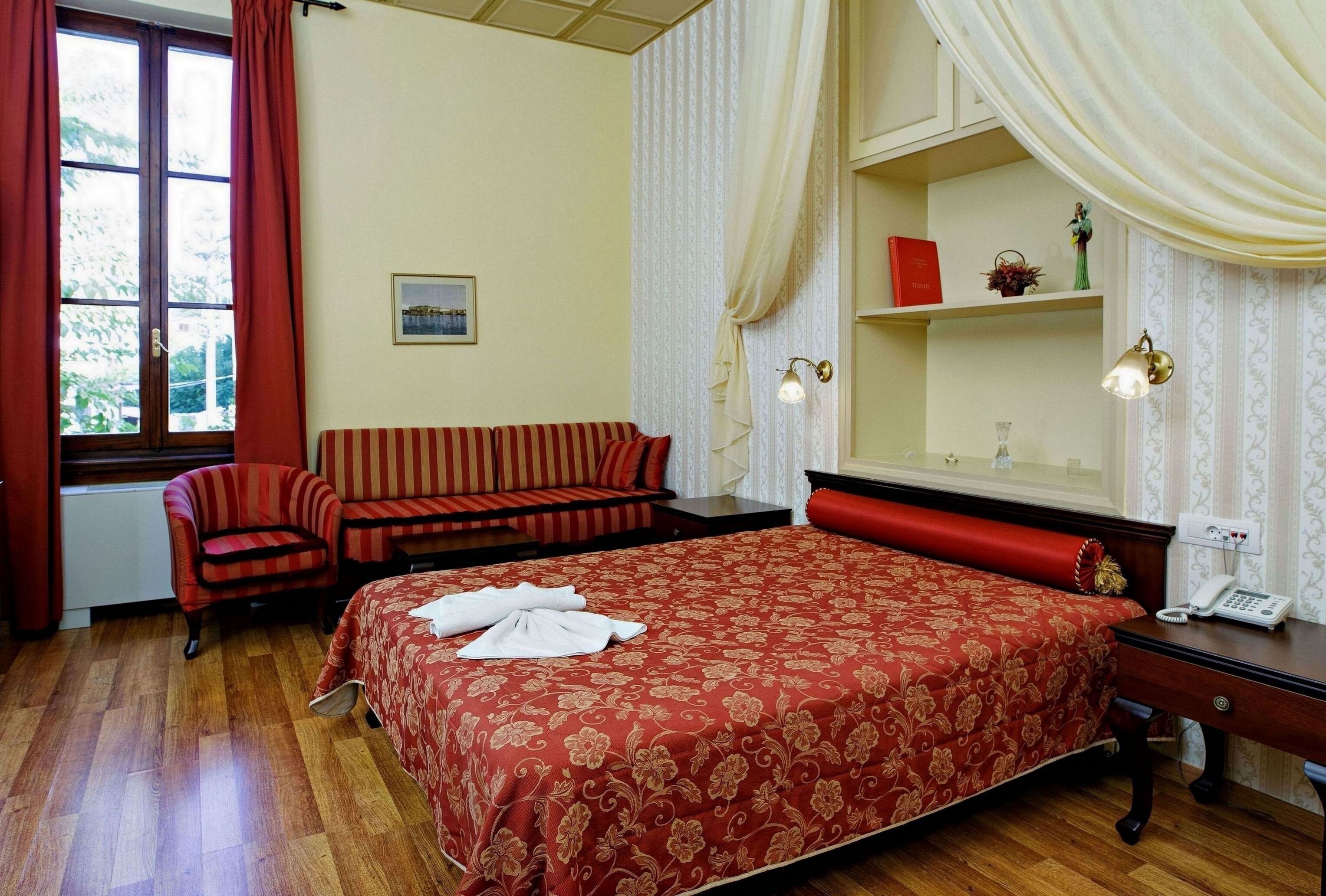 A hotel room with a large bed, a sofa, a chair, a desk with a telephone, and a window with curtains.