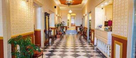 A hotel lobby with a checkered floor, a chandelier, and a reception desk.