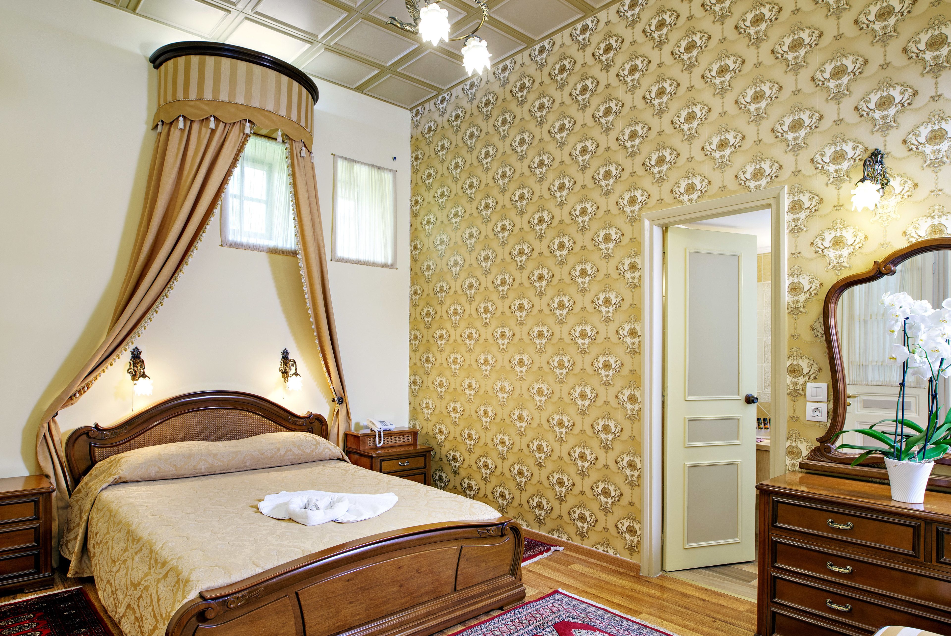 Ein Schlafzimmer mit einem Himmelbett, einer Holzkommode, einem Spiegel und einer Wand mit Muster.