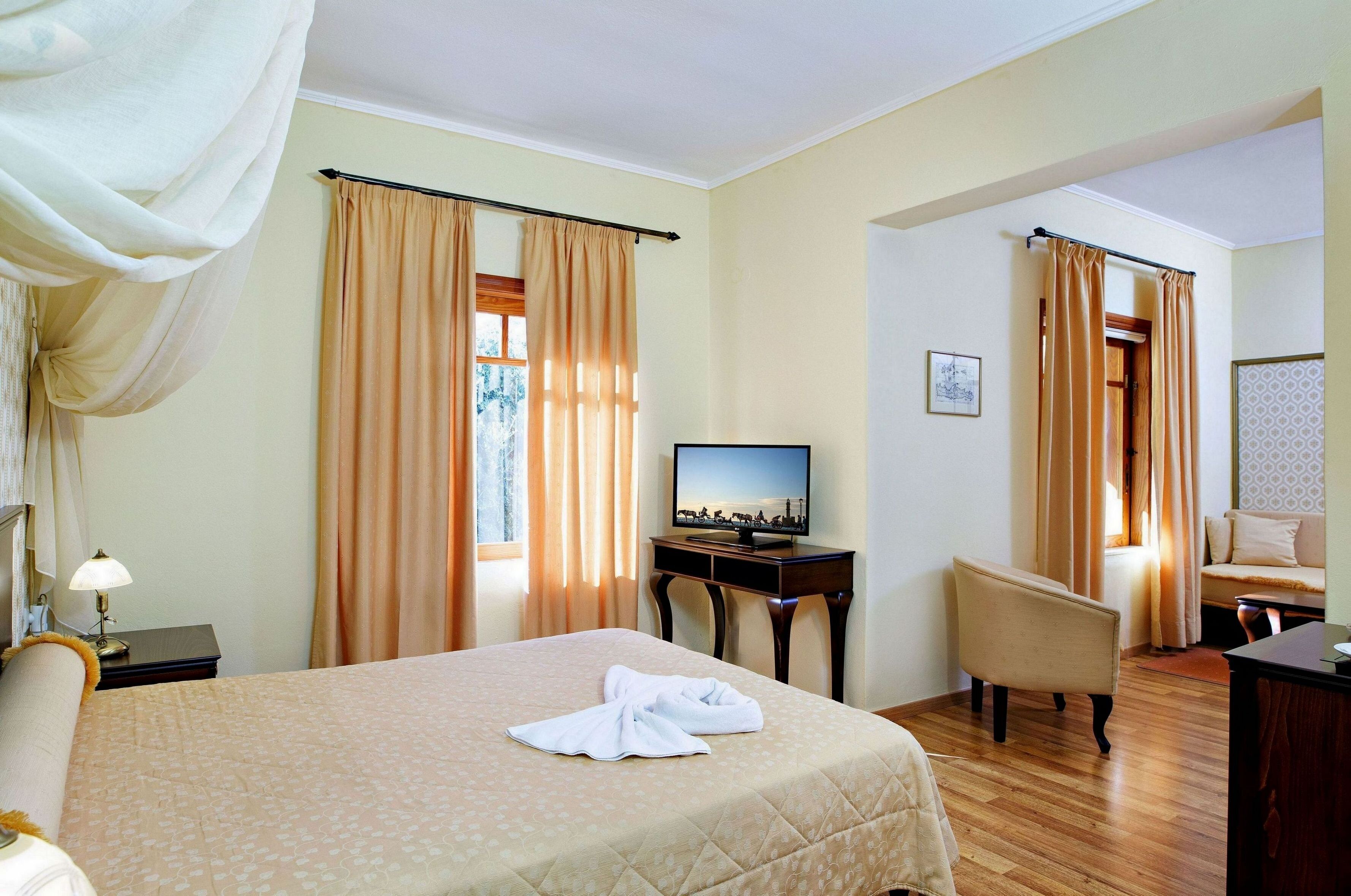 Una habitación de hotel con cama, televisión, escritorio, silla y cortinas.