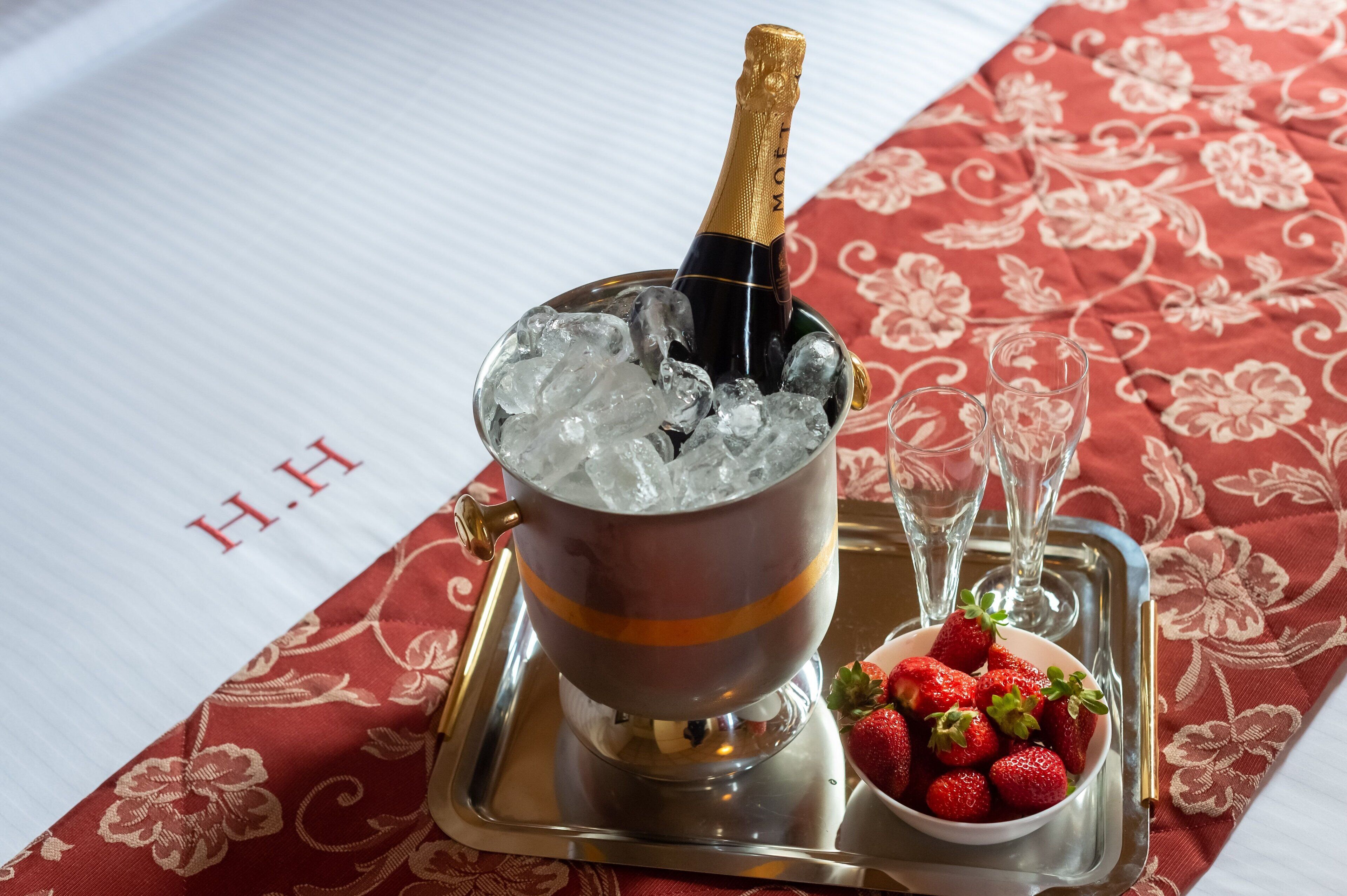 Eine Champagnerflasche in einem Eiskübel auf einem Tablett mit einer Schale Erdbeeren und zwei Gläsern.