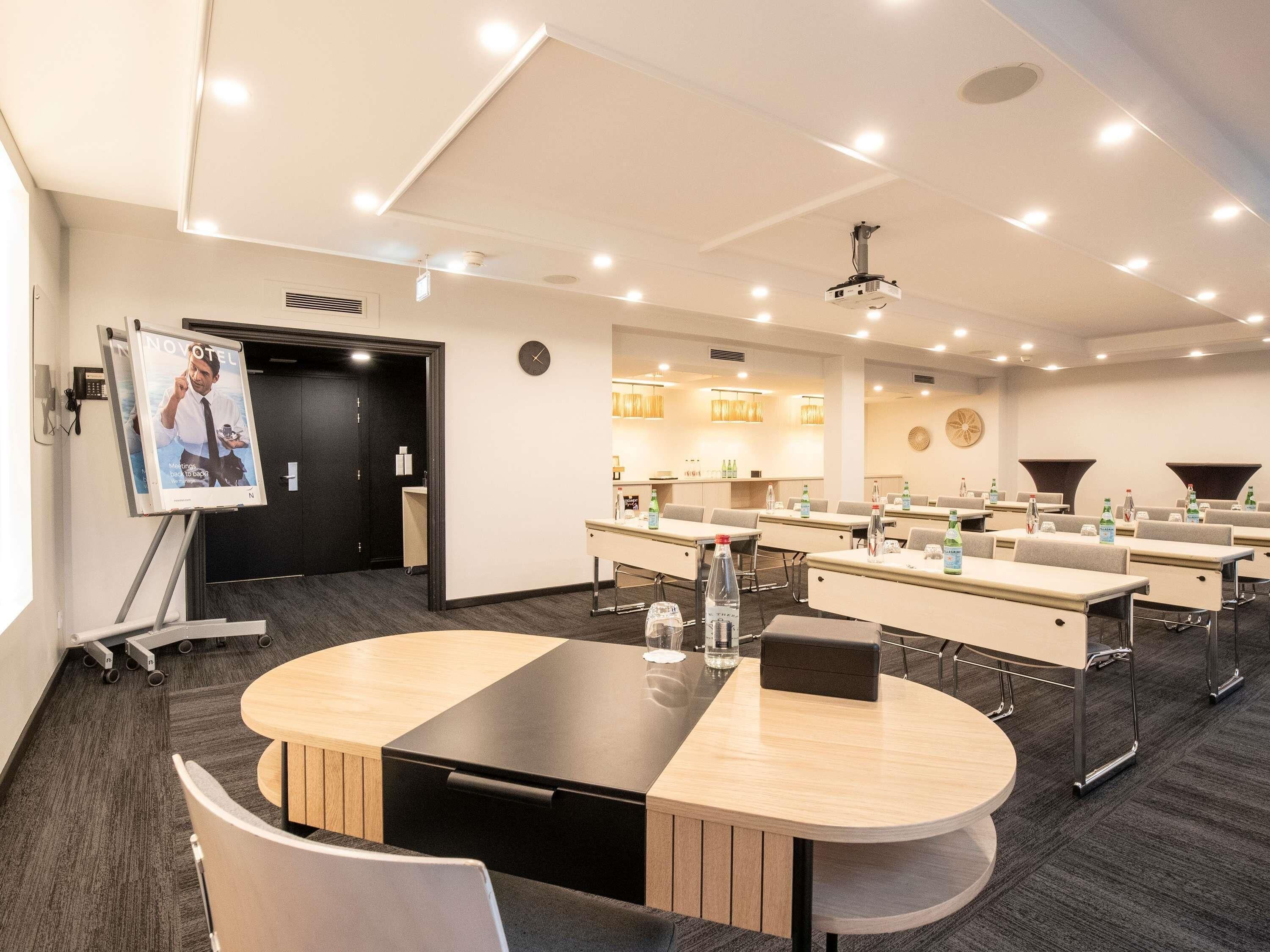 A conference room with a large table, chairs, a projector, and a clock on the wall.