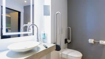A modern bathroom with a round sink, a mirror, a toilet, and a handrail.
