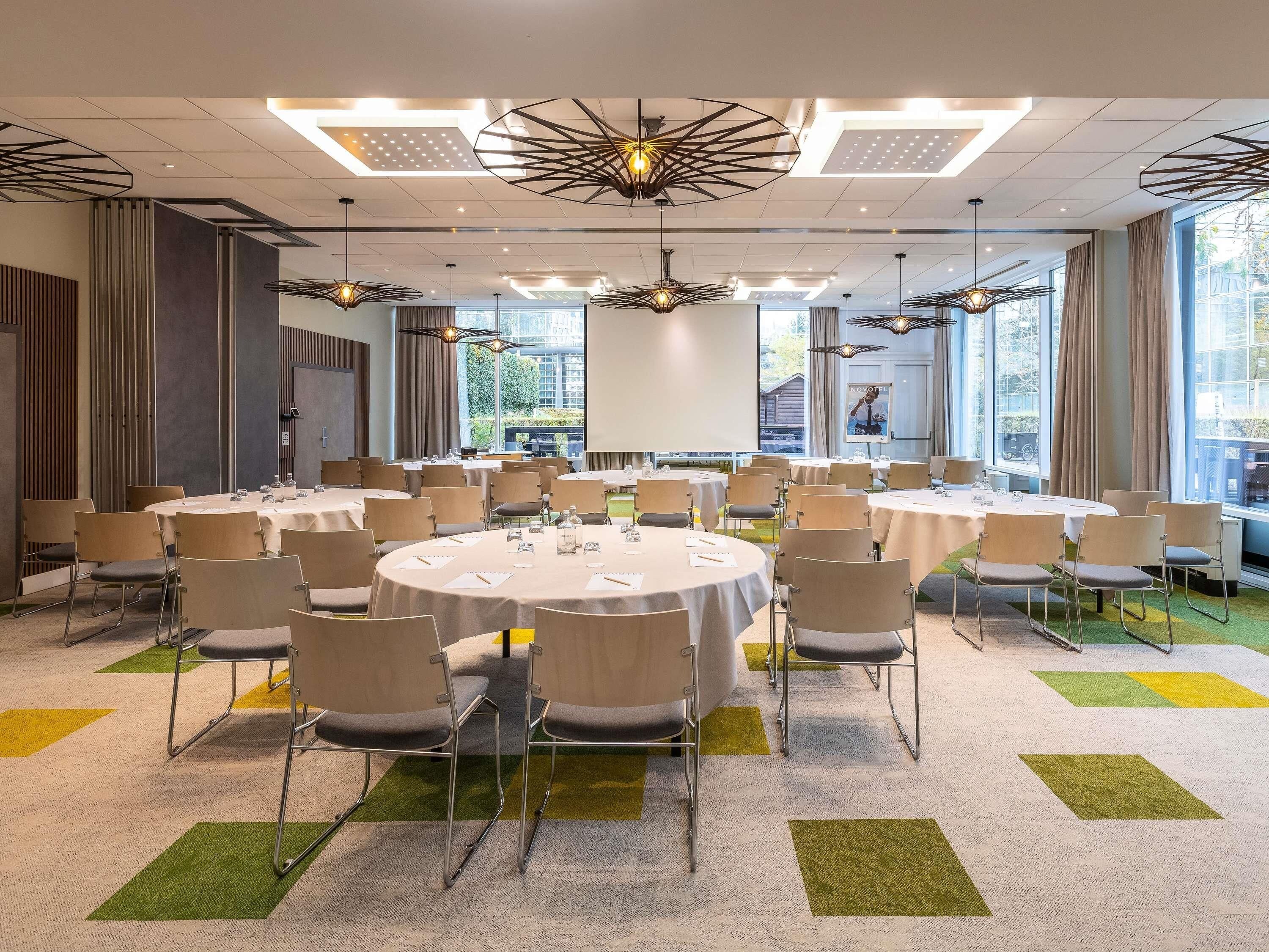 A conference room with round tables, chairs, and a projector screen.
