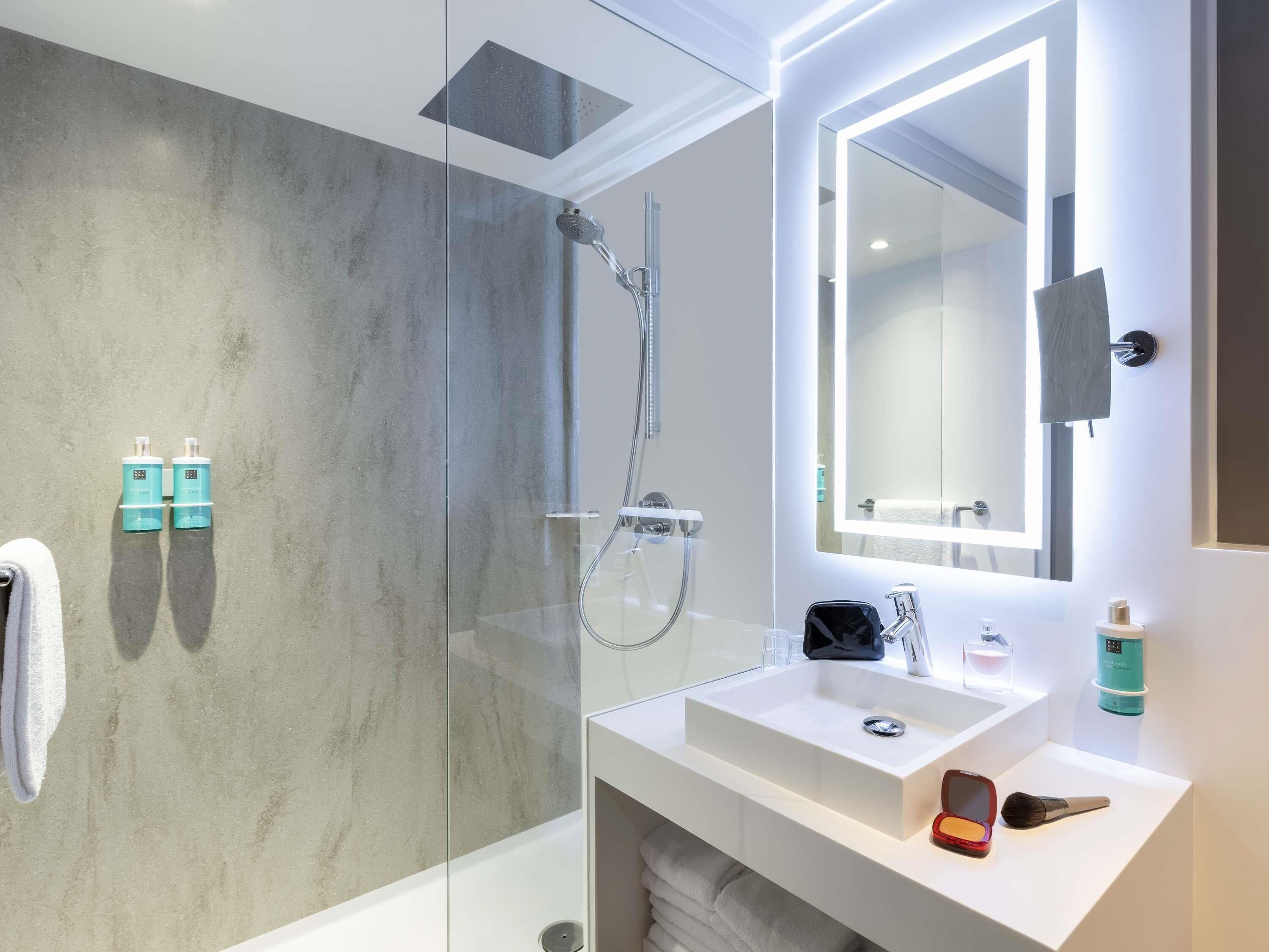 A modern bathroom with a glass shower enclosure, a white sink, and a large mirror.