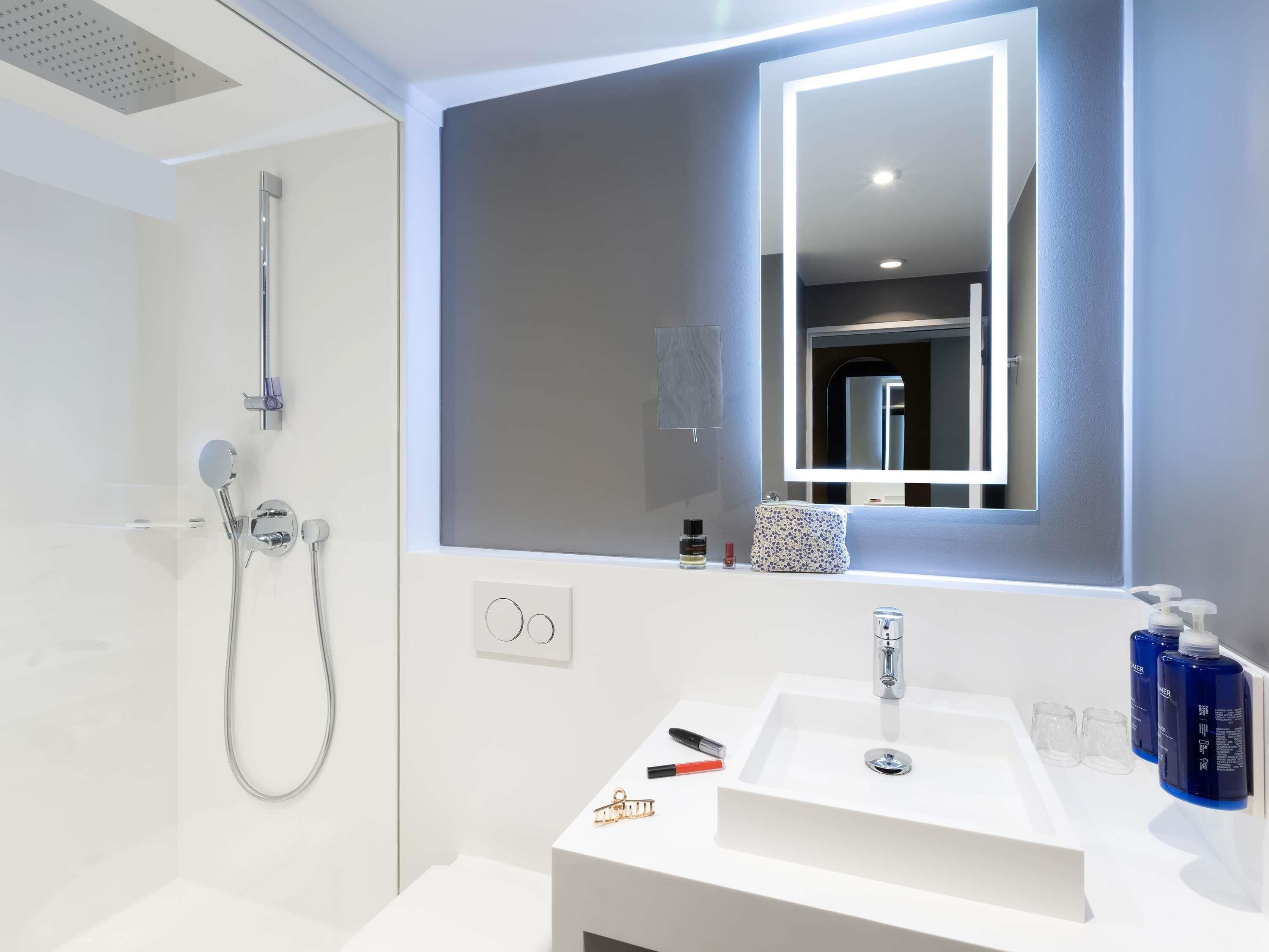 A modern bathroom with a walk-in shower, a large mirror, and a white sink with toiletries.