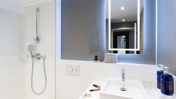 A modern bathroom with a walk-in shower, a large mirror, and a white sink with toiletries.
