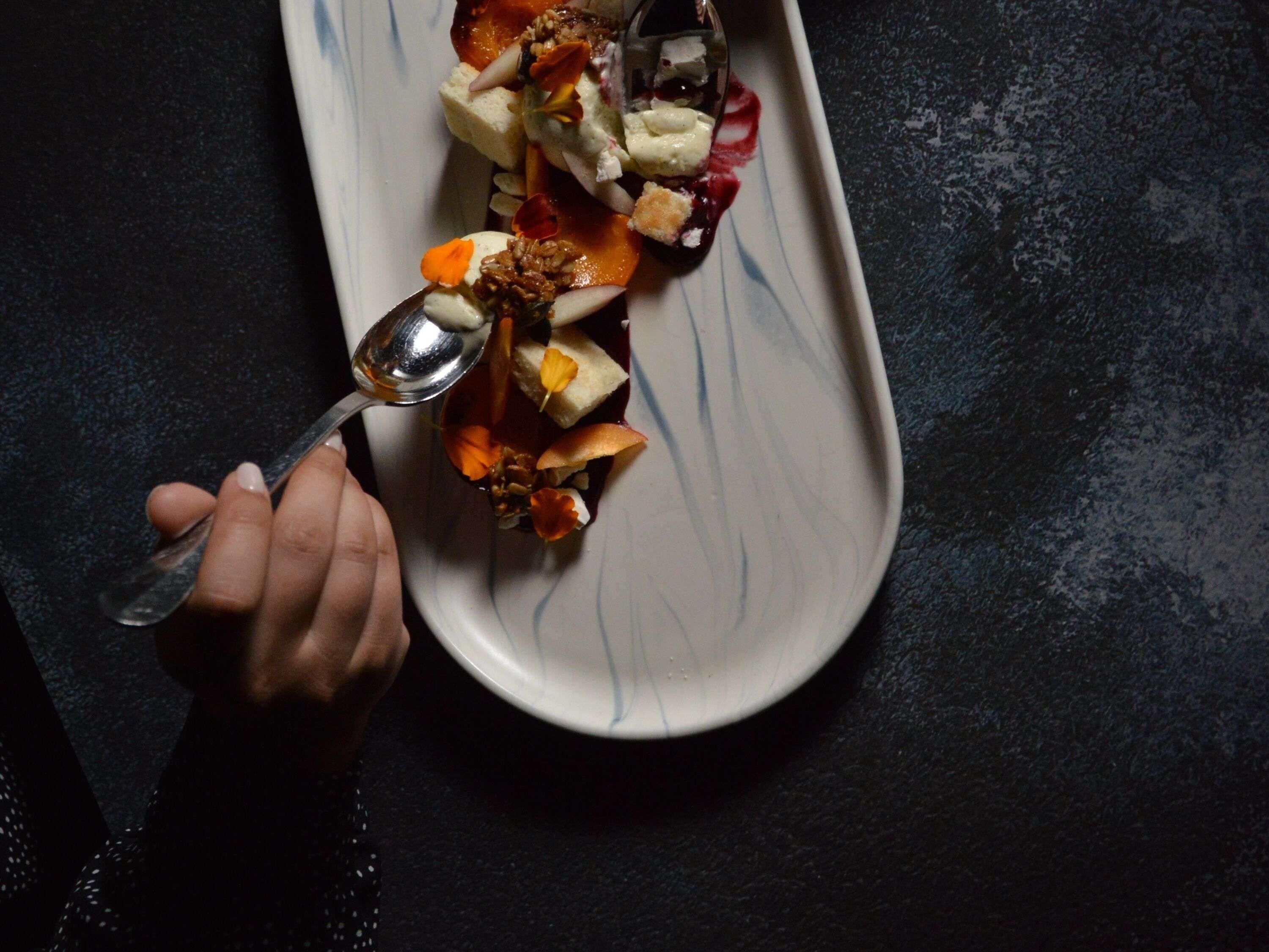 A hand holding a spoon over a dish with various food items on a plate.