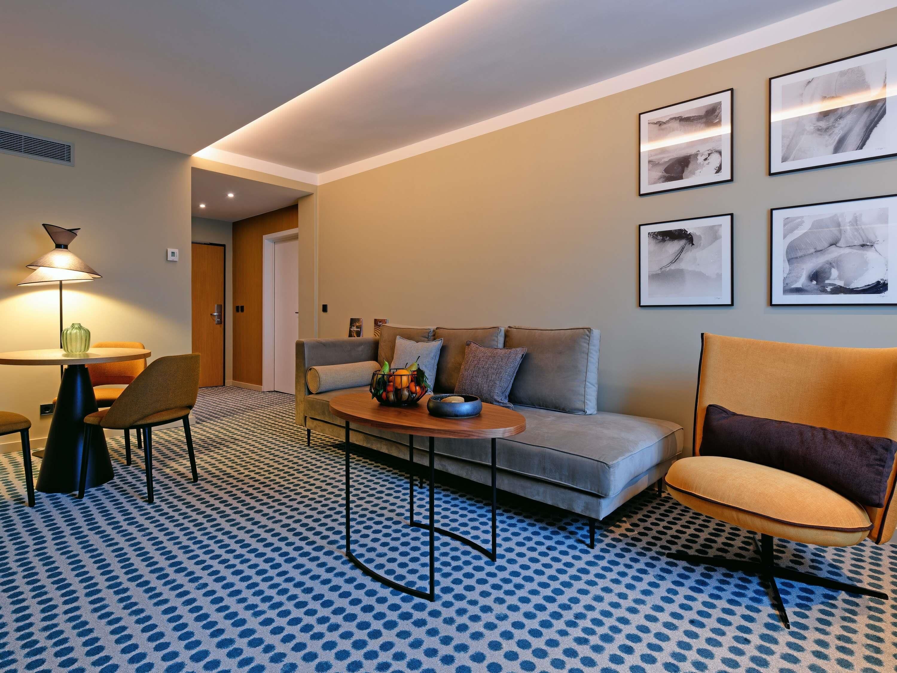 Una habitación de hotel moderna con sofá, sillones, una mesa de centro y obras de arte en las paredes.