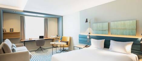 Et moderne hotelværelse med en stor seng, et skrivebord, en stol og en sofa.