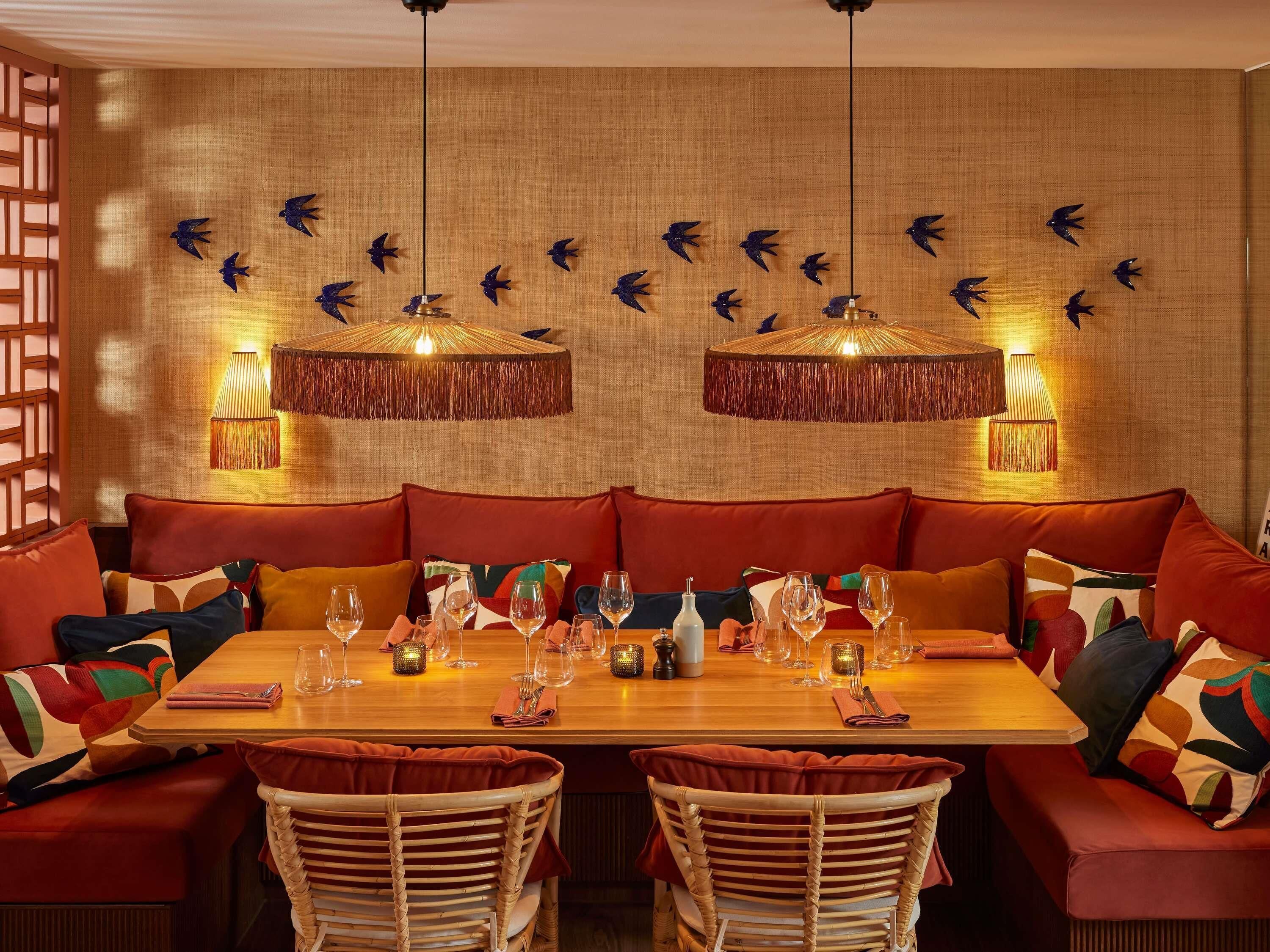 A dining area with a wooden table set for two, surrounded by wicker chairs and red upholstered seating.