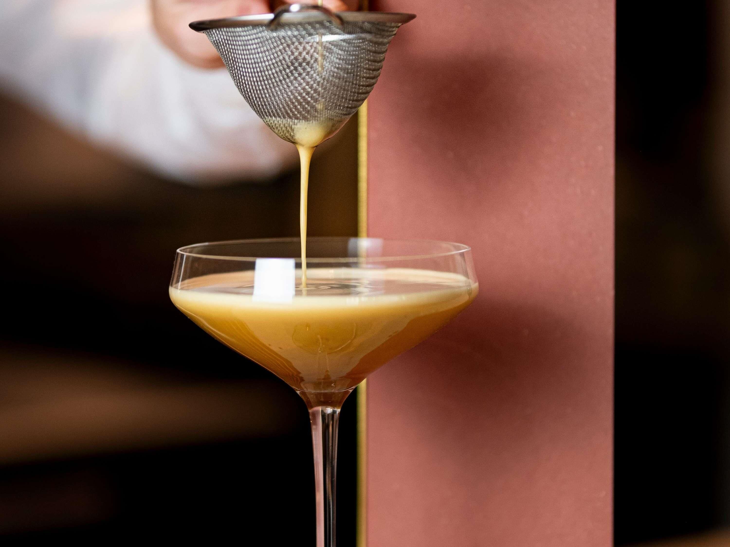 A martini glass with a clear liquid being poured into it.