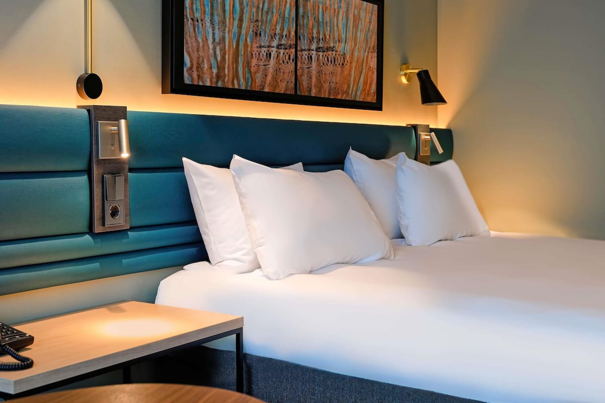 A modern hotel room with a large bed, a bedside table with a telephone, and a wall-mounted artwork.