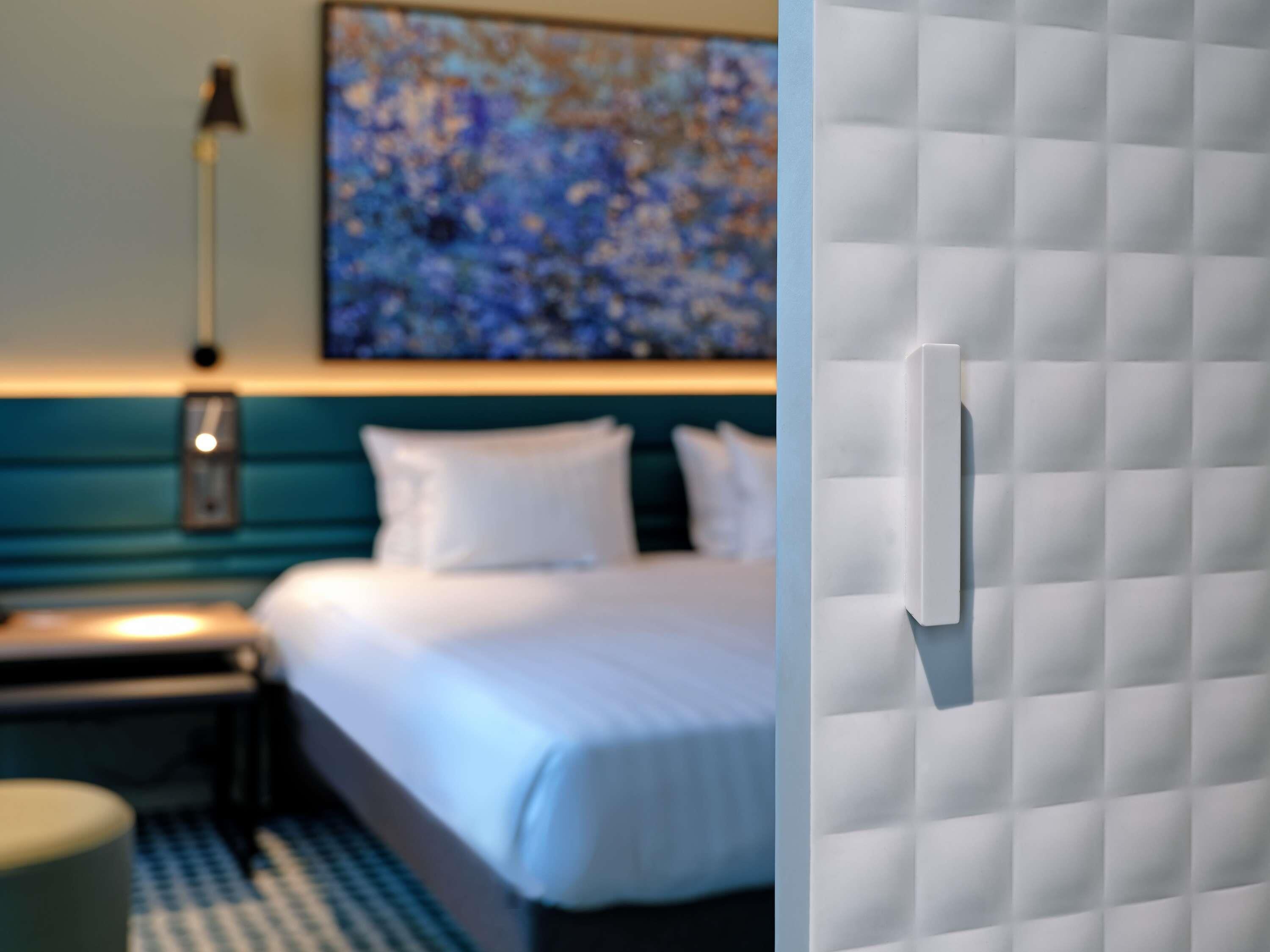 A hotel room with a bed, a nightstand, a lamp, and a painting on the wall.