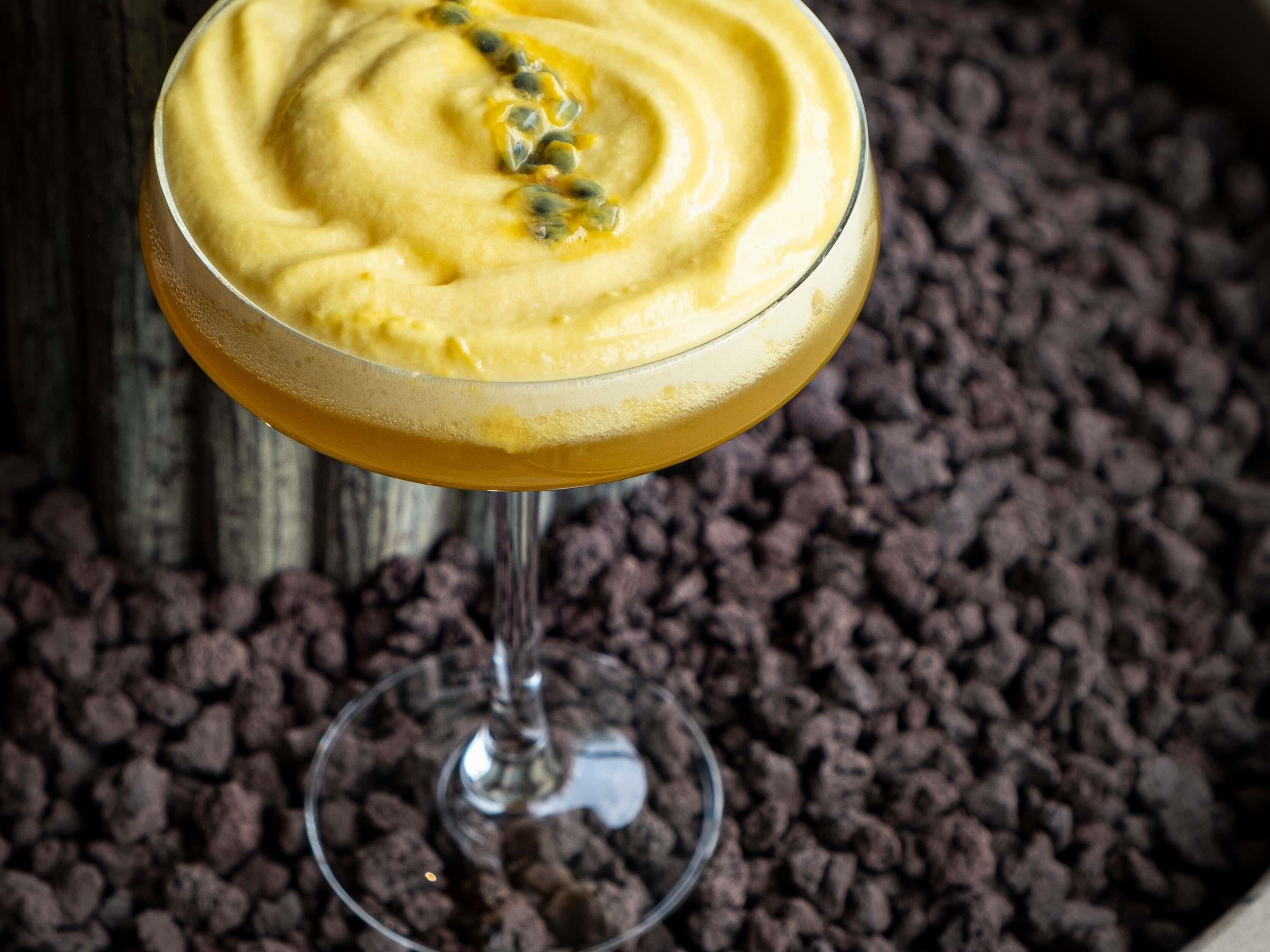 En cocktail i et glas med cremet konsistens og pynt, foran en baggrund af chokoladestykker.