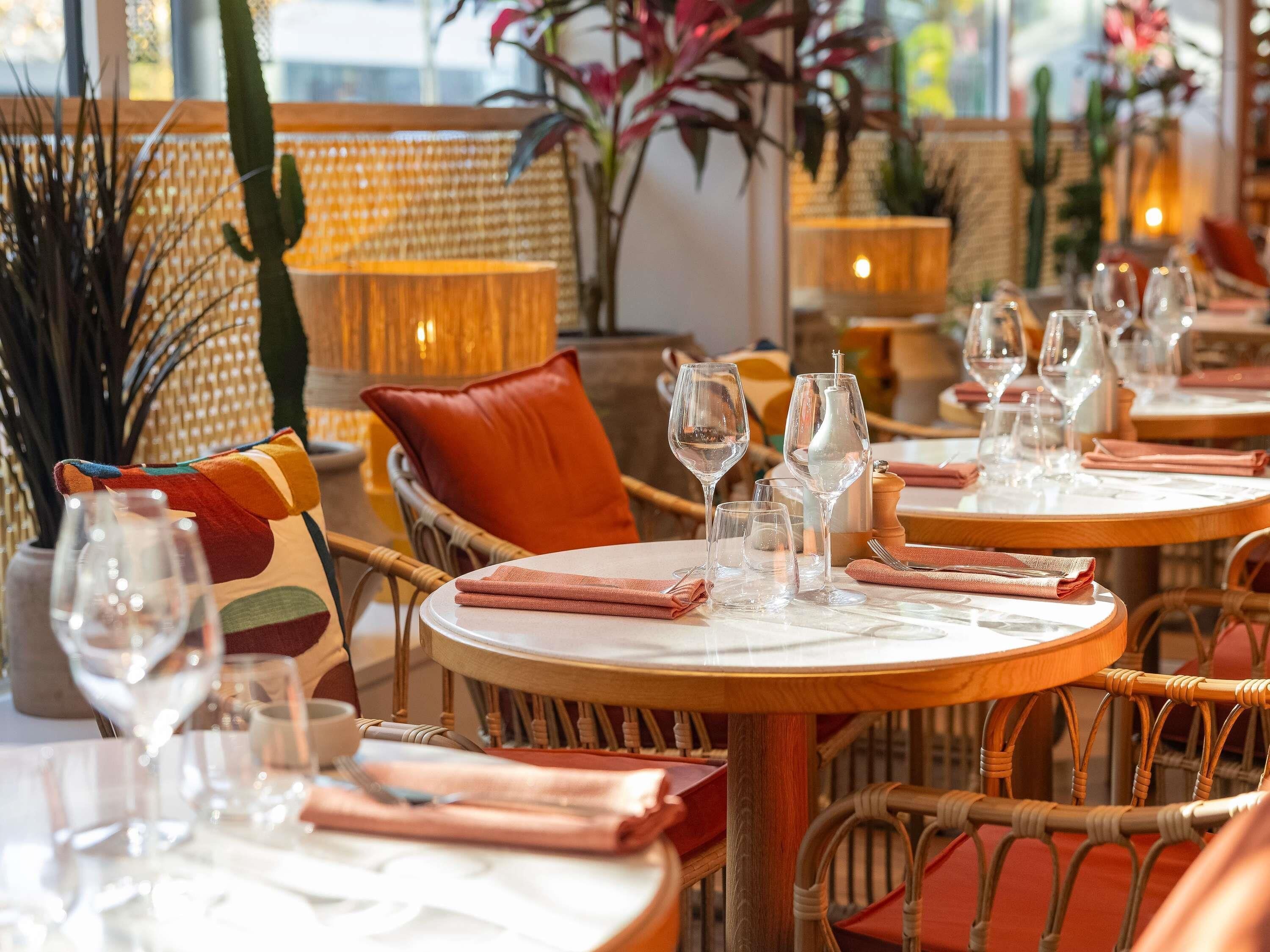A restaurant interior with round tables, wicker chairs, and a warm ambiance.