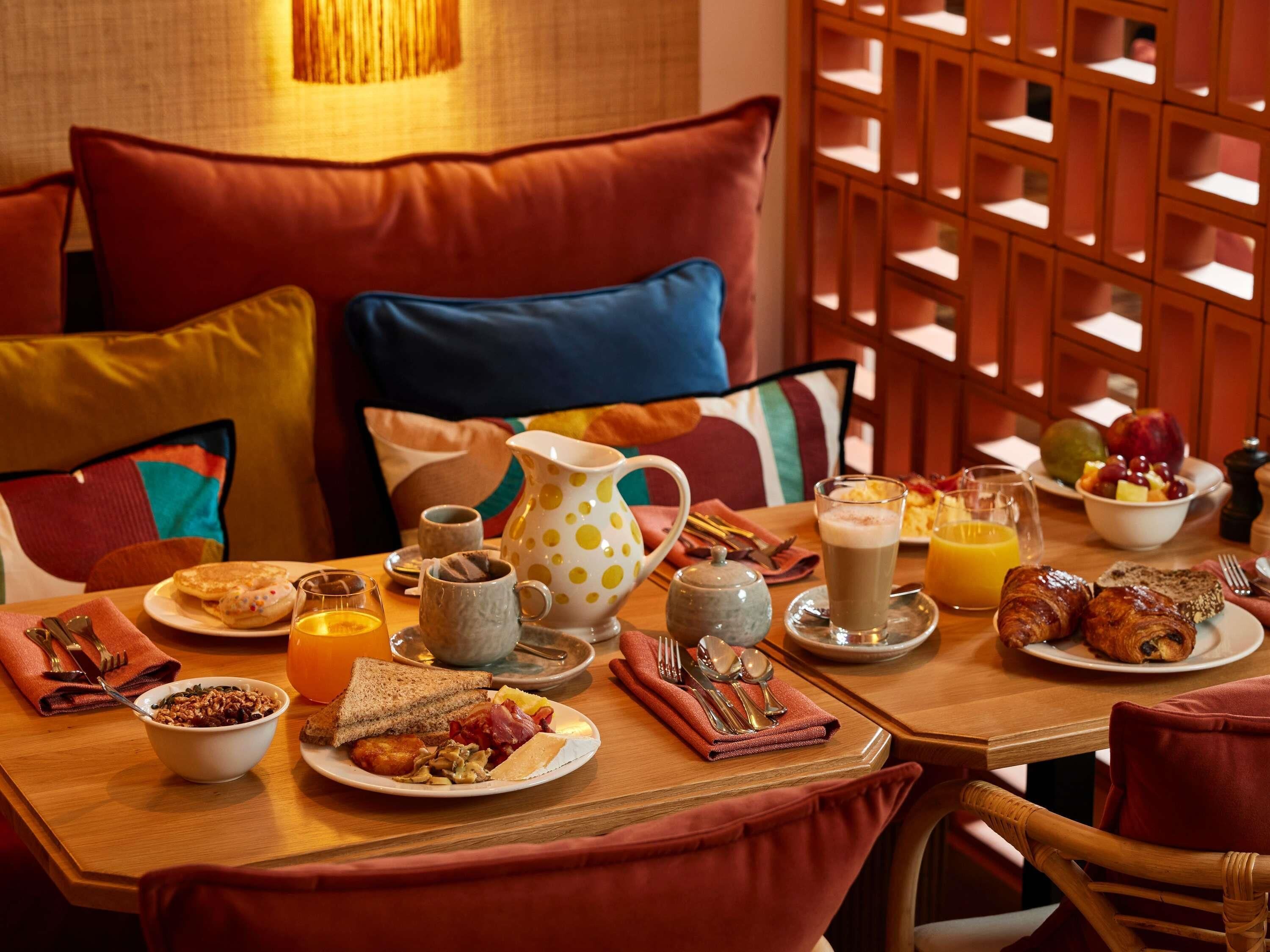 A breakfast setting with a variety of dishes, including toast, eggs, and fruit, on a wooden table.