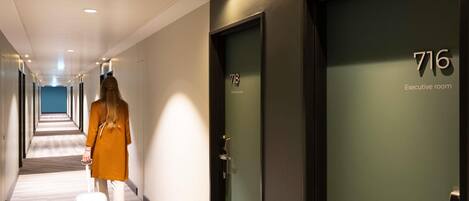A hotel corridor with a person walking with a suitcase, doors numbered 718 and 716, and an "Executive room" sign.