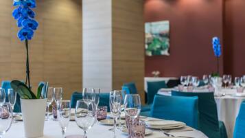 Comedor con mesas dispuestas para una comida, con orquídeas azules en jarrones blancos.