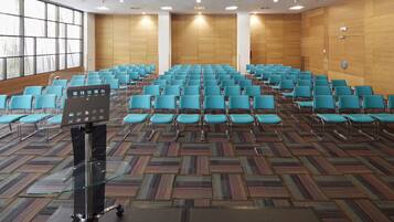 Un salón de conferencias con filas de sillas azules, una mesa de cristal y alfombra estampada.