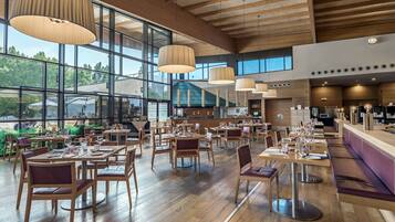 A spacious restaurant with wooden floors, large windows, and pendant lighting. Tables are set with wine glasses and plates.