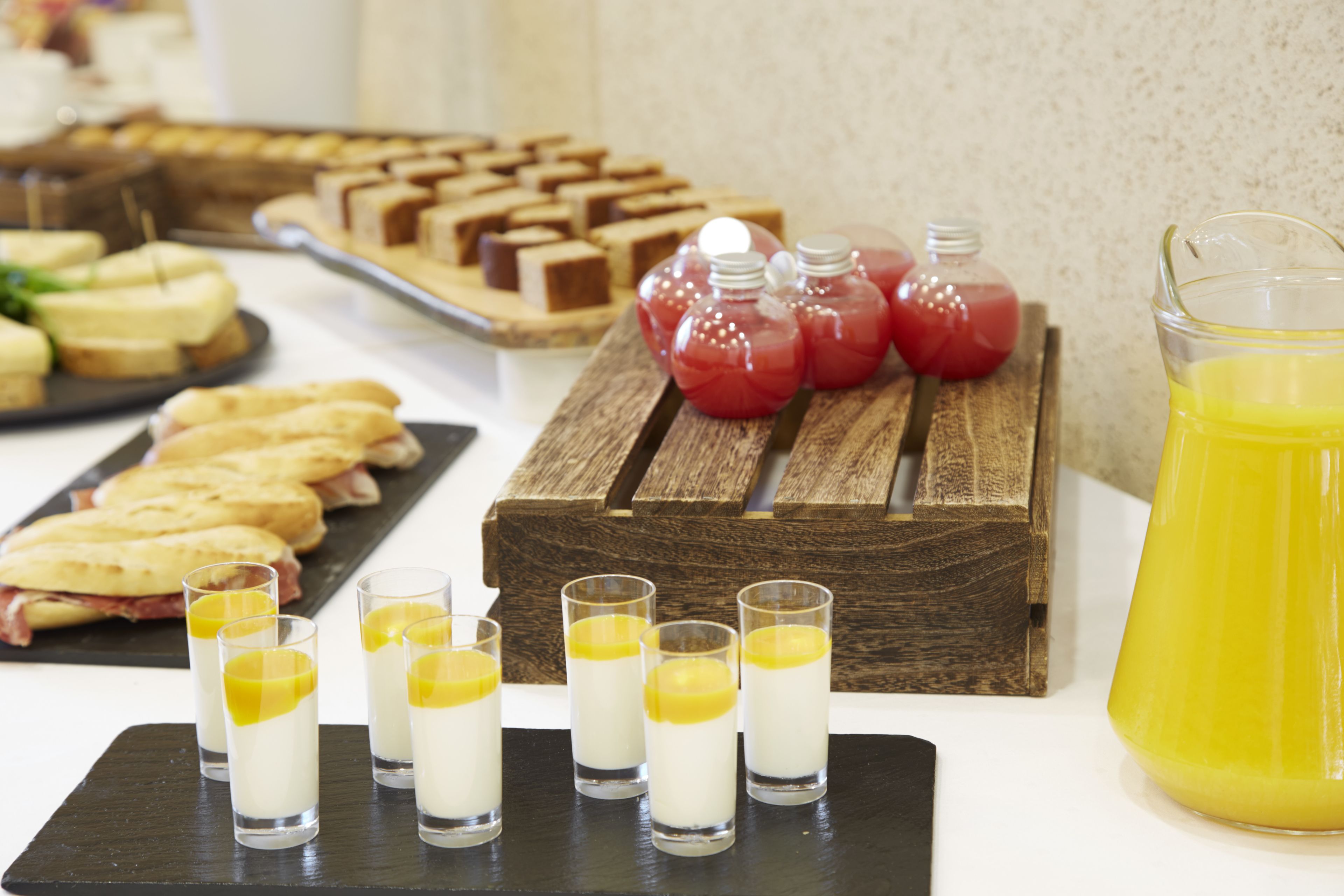 Ein reichhaltiges Buffet mit verschiedenen Speisen, darunter Sandwiches und Desserts, sowie ein Krug Orangensaft.