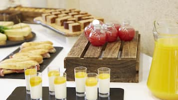 Ein reichhaltiges Buffet mit verschiedenen Speisen, darunter Sandwiches und Desserts, sowie ein Krug Orangensaft.