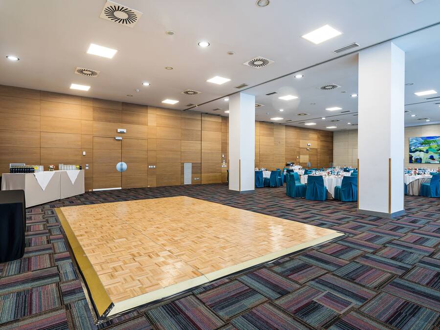 A spacious hall with a large wooden dance floor, multiple tables set for dining, and a modern ceiling design.