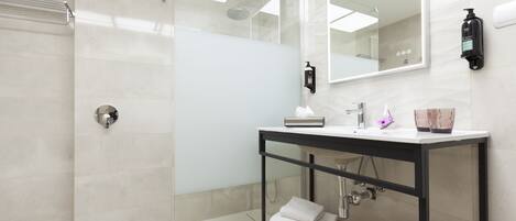 Un baño moderno con ducha envuelta en cristal, un lavabo blanco sobre encimera negra y un espejo grande.