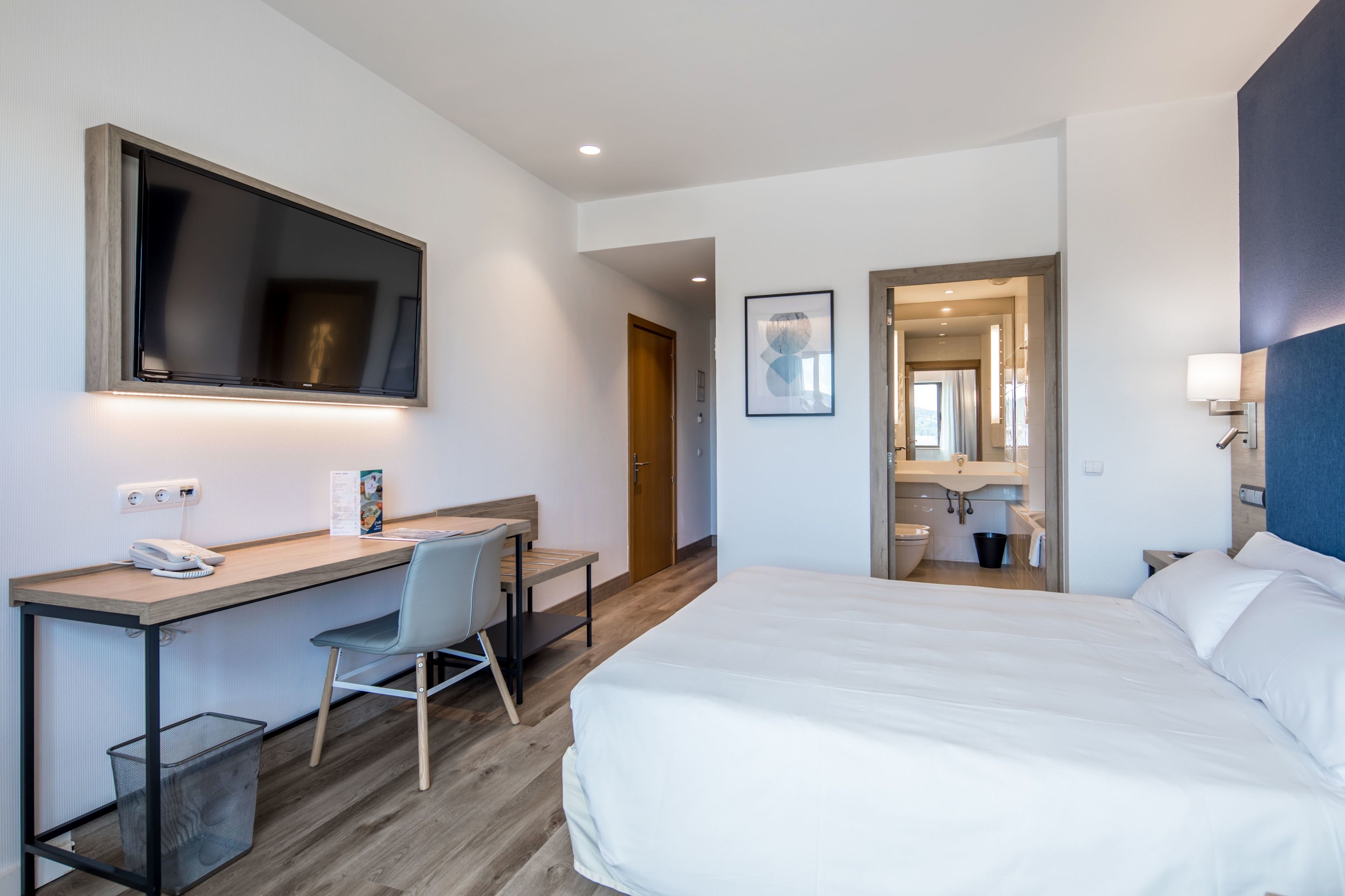 Habitación de hotel moderna con una cama grande, un escritorio con una silla, un cubo de basura pequeño y un espejo.