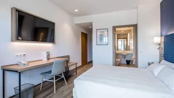 Habitación de hotel moderna con una cama grande, un escritorio con una silla, un cubo de basura pequeño y un espejo.