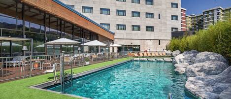 A swimming pool with a wooden deck and lounge chairs, surrounded by large rocks.