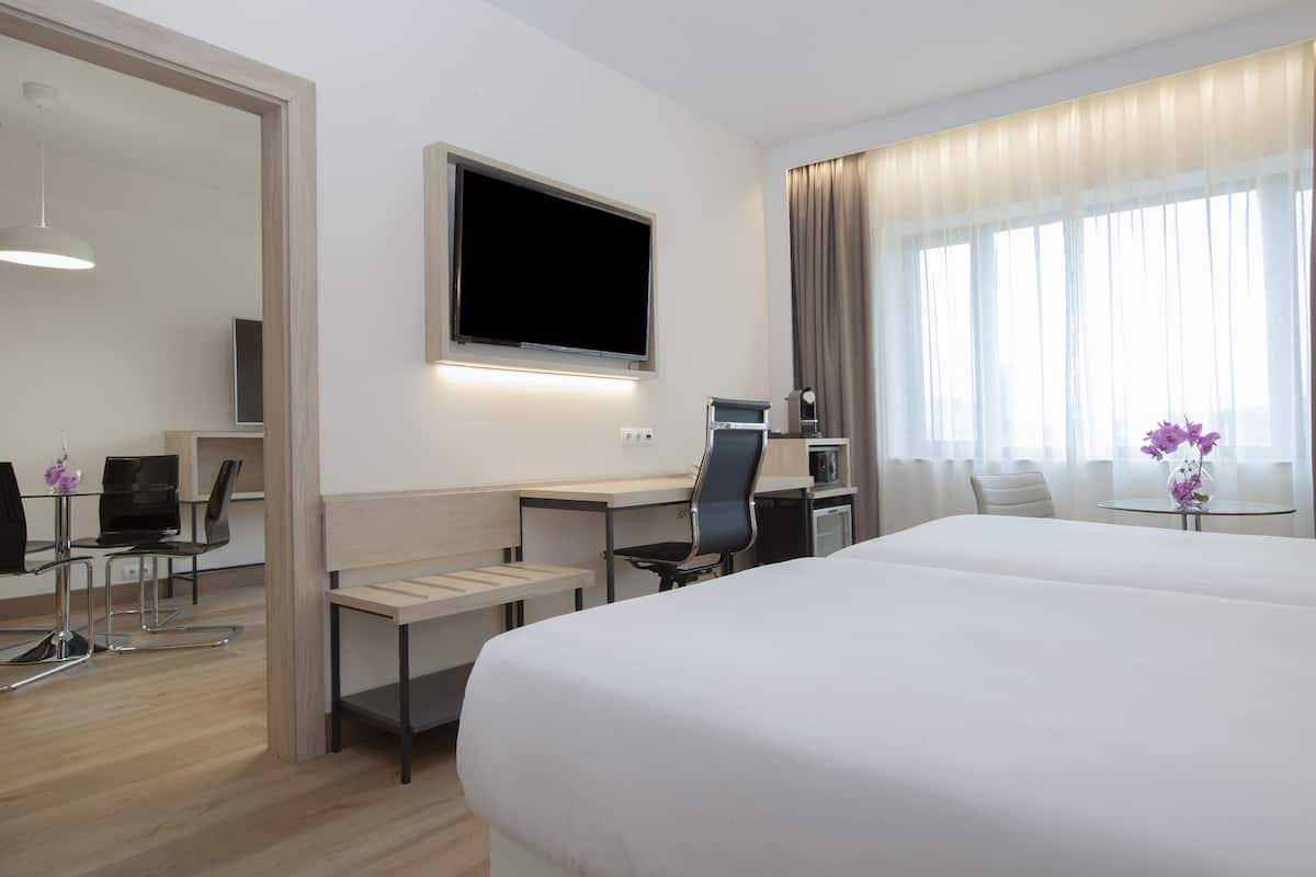 A hotel room with a bed, a desk with a chair, a television, and a window with curtains.