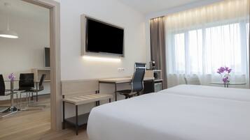 A hotel room with a bed, a desk with a chair, a television, and a window with curtains.