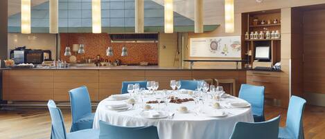 A modern dining area with a round table set for six, blue chairs, and a kitchen visible in the background.