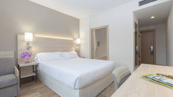 Een hotelkamer met een bed, een bureau, een stoel, een nachtkastje en een wandlamp.