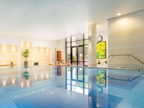 A spacious indoor swimming pool with clear glass walls, a wooden floor, and a modern interior design. - Novotel Paris Roissy CDG Convention (Roissy-en-France)